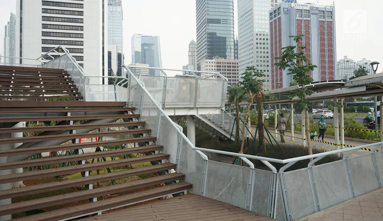Pejalan kaki melewati proyek pembangunan Taman Dukuh Atas di Jalan Jenderal Sudirman, Jakarta, Jumat (2/8/2019). Pembangunan ruang terbuka baru di Dukuh Atas ini diharapkan menjadi ruang bagi pejalan kaki dan lokasi berpindah moda transportasi. (Liputan6.com/Immanuel Antonius)