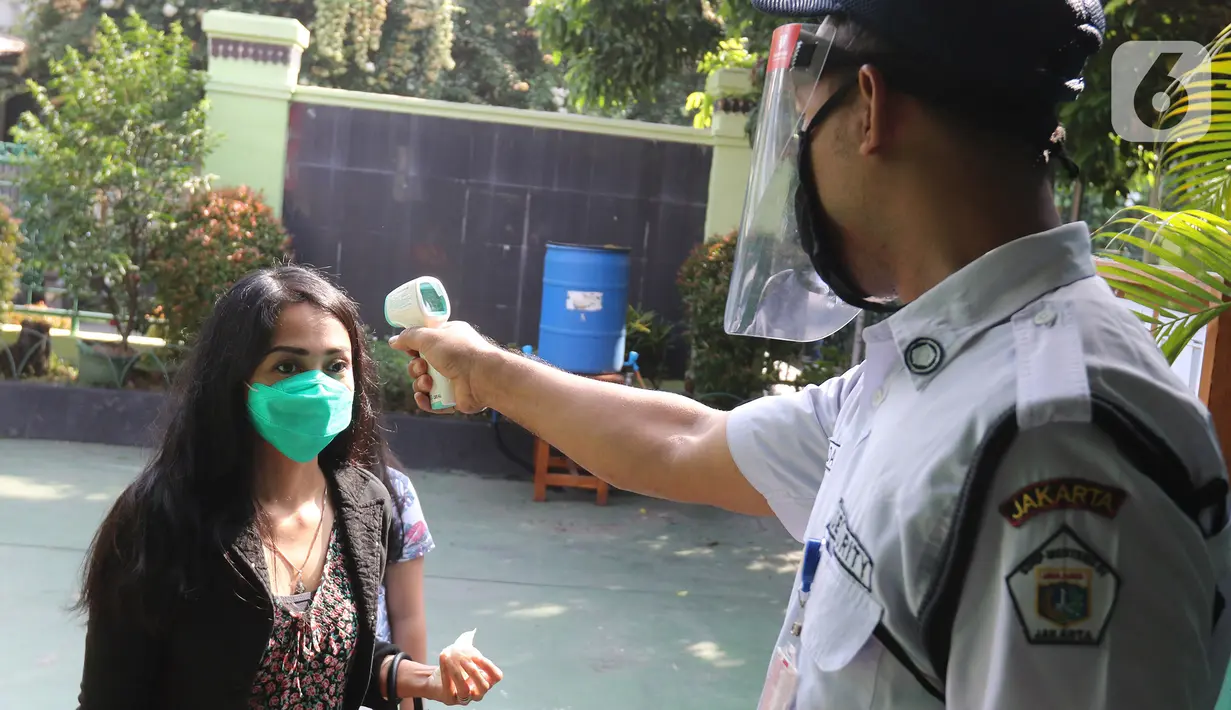 Petugas mengukur suhu wali murid sebelum pembagian laporan hasil belajar (rapor) kenaikan kelas di SD Negeri Menteng 01 Jakarta, Kamis (25/6/2020). Pembagian dilaksanakan mengikuti protokol kesehatan COVID-19 serta membagikan rapor secara bertahap dari 24-26 Juni 2020. (Liputan6.com/Herman Zakharia)