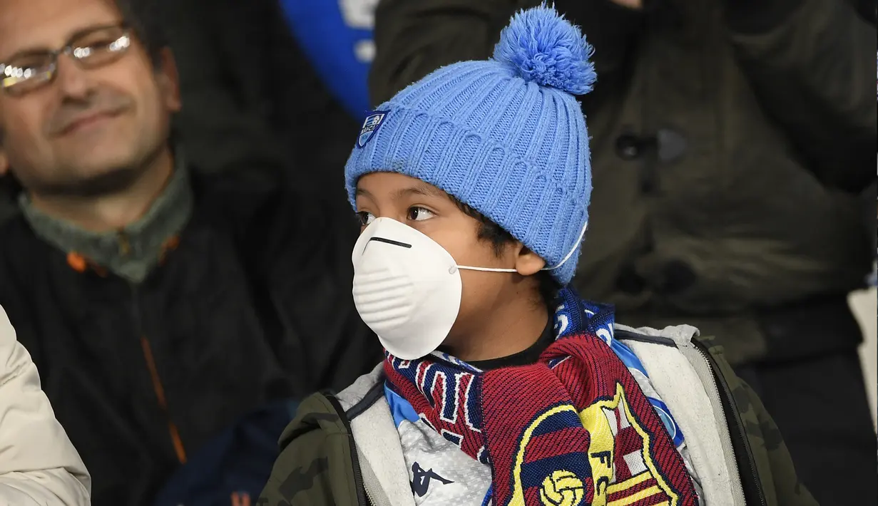 Seorang anak mengenakan masker menunggu dimulainya pertandingan antara Napoli dan Barcelona di Stadion San Paolo di Naples, Italia, Selasa, (25/2/2020). Sedikitnya tujuh pasien virus corona di Italia dilaporkan meninggal dunia. (AFP Photo/Filippo Monteforte)