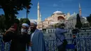 Orang-orang berswafoto dengan latar belakang Hagia Sophia di distrik bersejarah Sultanahmet di Istanbul, 11 Juli 2020. Berubahnya status bangunan yang memiliki kubah ikonik ini menjadi masjid tentu membuat publik heboh. (AP Photo/Emrah Gurel)