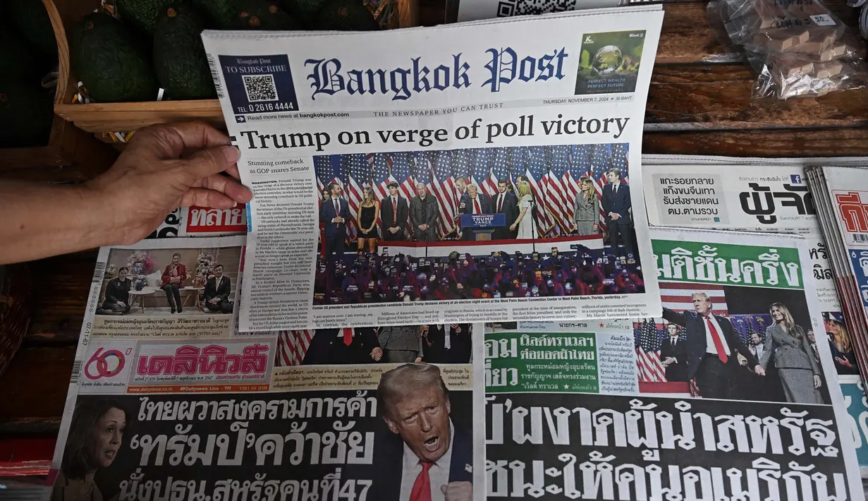 Sebelumnya, berdasarkan penghitungan cepat, Donald Trump berhasil memenangi Pemilihan Presiden Amerika Serikat (AS) 2024 setelah berhasil meraih 294 suara dari total 538 suara elektoral. Sementara, Kamala Harris meraih 223 suara elektoral. Tampak dalam foto, seorang pedagang mengatur koran pagi lokal Bangkok Post, Dailynews, dan Thai Rath yang menunjukkan reaksi atas terpilihnya kembali Presiden AS terpilih Donald Trump, di Bangkok pada 7 November 2024. (Lillian SUWANRUMPHA/AFP)