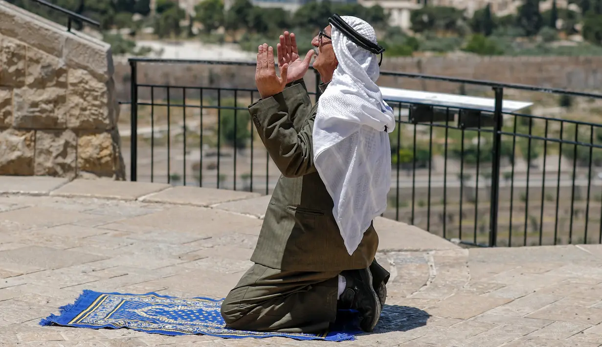 Seorang pria Palestina melaksanakan salat Jumat saat bulan Ramadan di depan Bukit Zaitun dengan latar belakang kota tua Yerusalem dan Masjid Al-Aqsa yang ditutup, Jumat (8/5/2020). Masjid Al-Aqsa telah ditutup sejak bulan lalu untuk mencegah penyebaran Covid-19. (Photo by AHMAD GHARABLI / AFP)