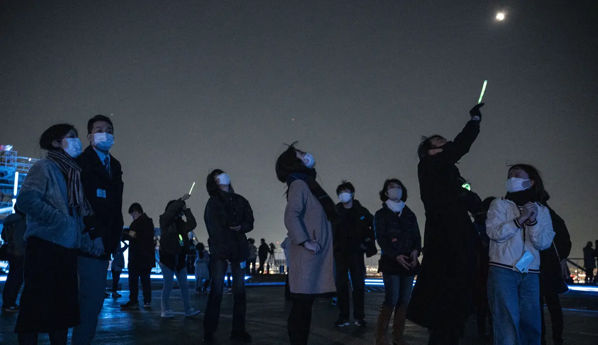 <p>Warga keluar untuk melihat gerhana bulan total "blood moon" di atas langit Tokyo dari atap gedung tinggi pada 8 November 2022. Fenomena alam tersebut dapat disaksikan dengan mata telanjang. (Photo by Richard A. Brooks / AFP)</p>