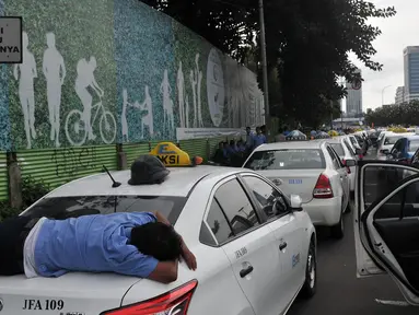 Seorang sopir tidur diatas bagasi taksi saat demo di depan Gedung DPR/MPR, Jakarta, Selasa (22/3). Selain melakukan demo, sopir taksi tersebut melakukan sweeping ke supir taksi yang beroperasi di dalam tol, dan membakar ban. (Liputan6.com/Johan Tallo)