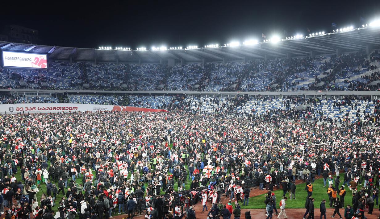 Suporter Timnas Georgia tumpah ruah turun kelapangan setelah timnya berhasil mengalahkan Yunani dalam laga playoff yang menegangkan di Tbilisi, Rabu (27/4/2024). Georgia sukses mencetak sejarah dengan lolos ke Euro 2024 untuk pertama kalinya. (AFP/Giorgi Arjevanidze)