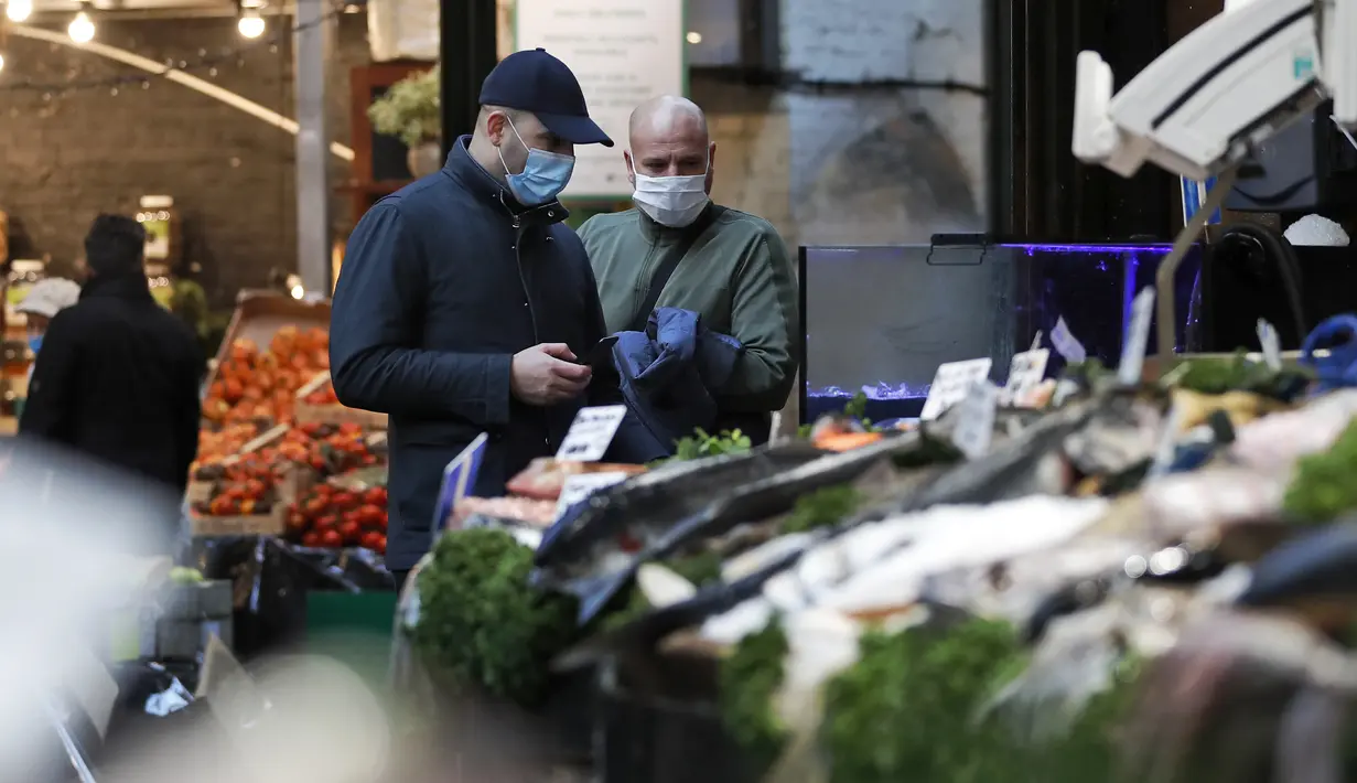 Orang-orang yang memakai masker wajah berbelanja di Borough Market di London selatan selama penguncian nasional (lockdown) ketiga Inggris, Selasa (12/1/2021). Borough Market menjadi tempat pertama yang mewajibkan pemakaian masker di luar ruangan. (AP Photo/Alastair Grant)