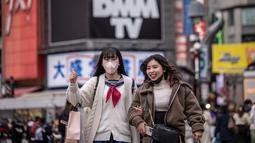 Dua perempuan menyeberang jalan di distrik Shibuya Tokyo pada hari pertama pemerintah Jepang mencabut ketentuan wajib mengenakan masker, Senin (13/3/2023).Meski kewajiban masker berakhir, tak mudah mengubah perilaku masyarakat yang sudah terbiasa menggunakan penutup wajah ini. (Photo by Yuichi YAMAZAKI / AFP)