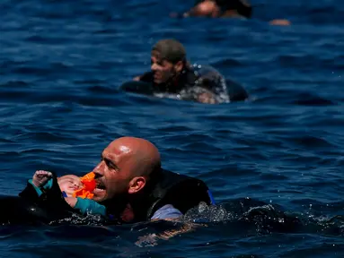Seorang pengungsi Suriah menggendong bayi sambil berenang menuju pantai setelah perahu yang mereka naiki kempes sebelum mencapai pulau Yunani Lesbos, 12 September 2015. (REUTERS/Alkis Konstantinidis)  