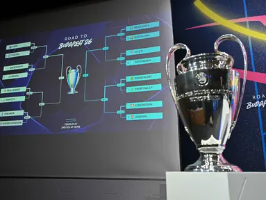 Foto menunjukkan Piala Liga Champions yang dipajang di samping layar yang menampilkan hasil undian babak 16 besar, perempat final, dan semifinal Liga Champions 2025/2026 di House of European Football di Nyon, Swiss, Jumat (27/2/2026). Pengundian laga babak 16 besar, perempat final, dan semifinal Liga Champions 2025/2026 di House of European Football di Nyon, Swiss, Jumat (27/2/2026). (Harold CUNNINGHAM/AFP)