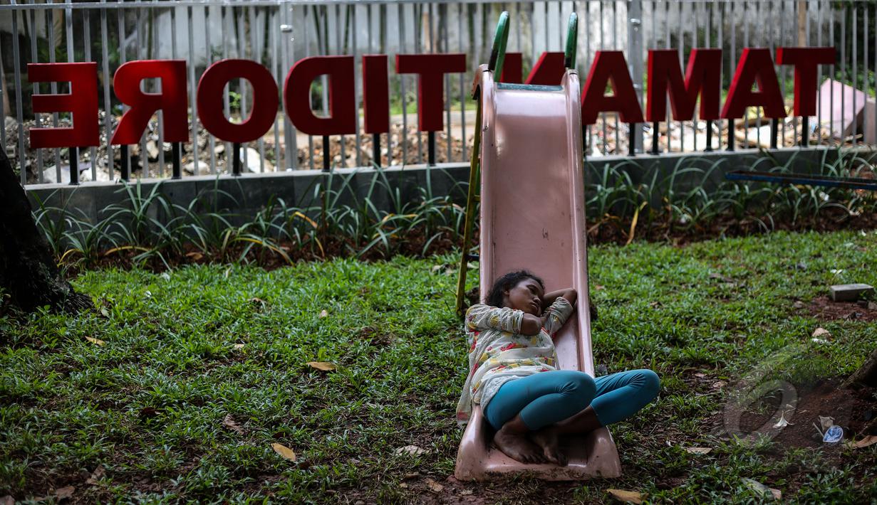Seorang warga tertidur di papan perosotan di tengah Proyek pembangunan Ruang Publik Terpadu Ramah Anak (RPTRA) di Jalan Tidore RW 05, Kelurahan Cideng, Gambir, Jakarta, Senin (4/5/2015). (Liputan6.com/Faizal Fanani)