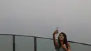 Seorang wanita berselfie dengan latar belakang pemandangan distrik pusat bisnis Singapura yang diselimuti kabut asap, Senin (14/9/2015). Singapura tak luput terkena dampak kabut asap pembakaran lahan di Pulau Sumatera. (REUTERS/Edgar Su)