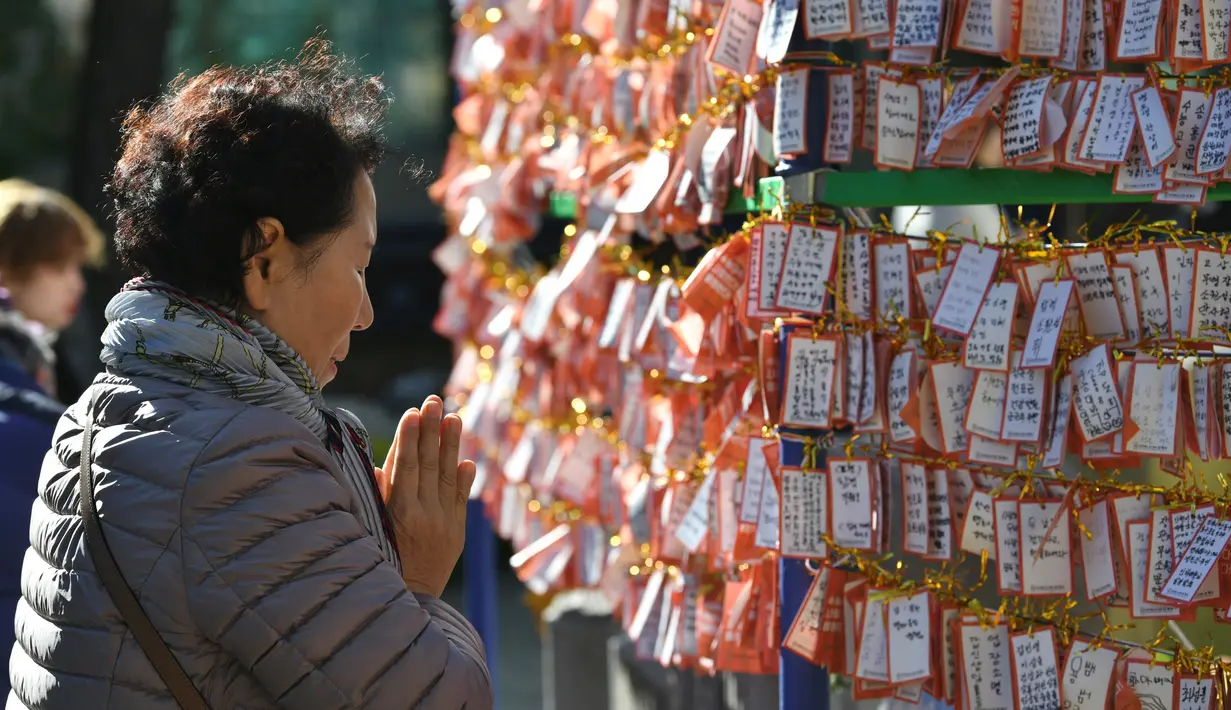 Seorang perempuan berdoa di depan deretan kertas untuk keberhasilan para siswa dalam ujian masuk perguruan tinggi di kuil Buddha Jogye, Seoul, Kamis (14/11/2019). Ujian masuk perguruan tinggi disebut-sebut sebagai ujian pertaruhan hidup para pelajar Korea Selatan. (Jung Yeon-je / AFP)