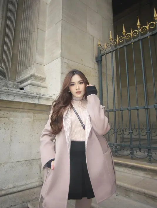 Penampilan menawan Mahalini dengan coat dan knit top serba warna nude saat berpose di depan museum Louvre Paris. [@mahaliniraharja]