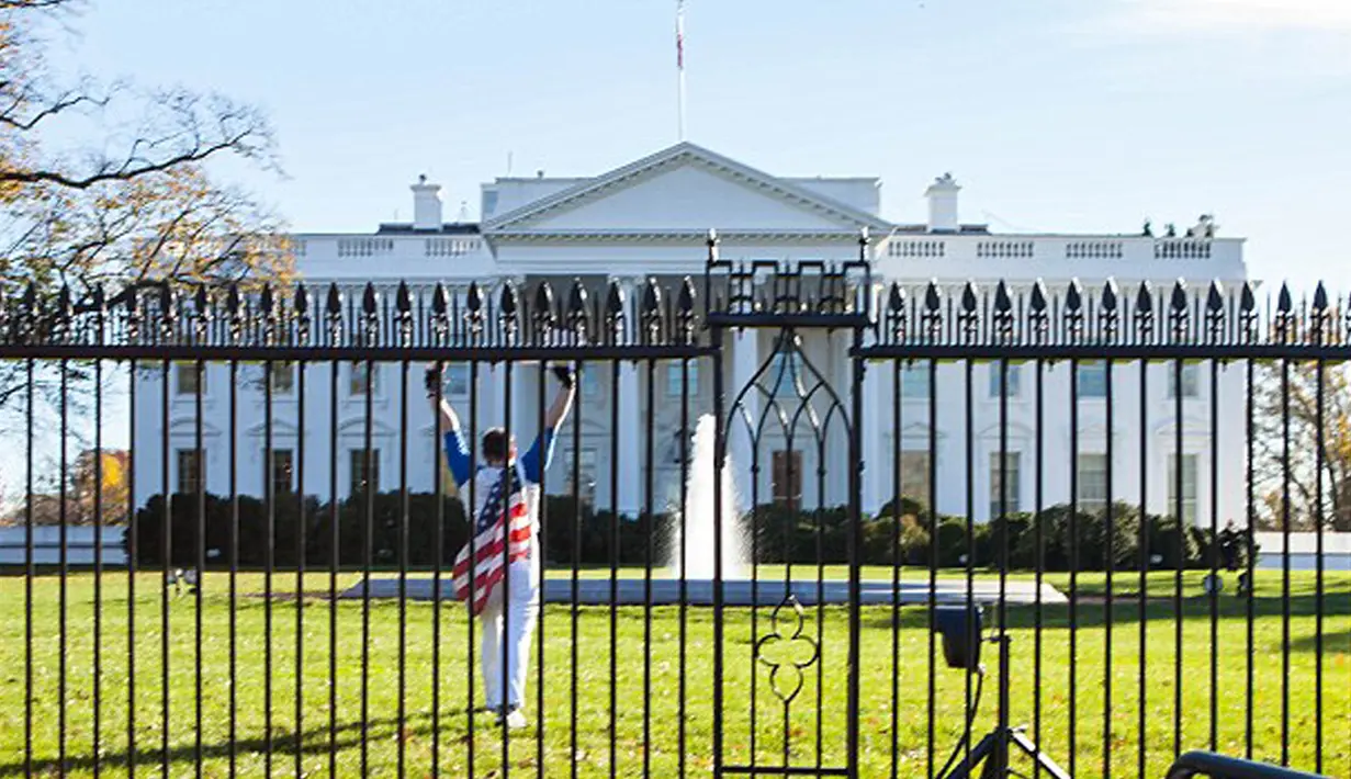Pria berselimut bendera Amerika tampak mengangkat tangannya usai melompati pagar Gedung Putih di Washington, Kamis (26/11). Insiden itu terjadi saat Presiden AS Barack Obama sedang berada di dalam Gedung Putih merayakan hari Thanksgiving (dailymail.co.uk)