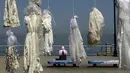 Seorang wanita duduk dekat puluhan gaun pengantin yang digantung di tepi pantai Beirut, Sabtu (22/4). Gaun yang digantung di tepi pantai itu sebagai bentuk protes Undang-Undang Pemerkosaan di Lebanon oleh sekelompok aktivis. (PATRICK BAZ/AFP)