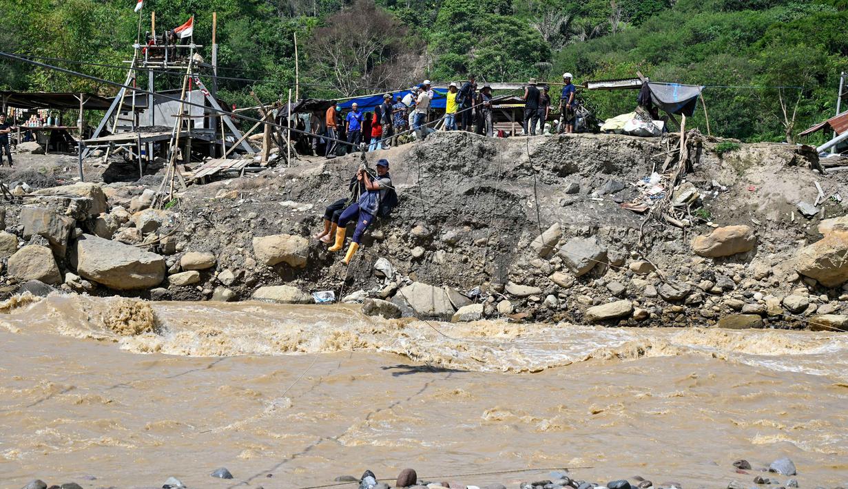 Tali sling menjadi satu-satunya penghubung antar desa yang terpisah oleh sungai berarus deras. Tampak dalam foto, warga menggunakan tali untuk menyeberangi sungai setelah banjir bandang yang menghancurkan desa-desa di sekitarnya di Ketol, provinsi Aceh, pada Selasa 6 Januari 2026. (CHAIDEER MAHYUDDIN/AFP)