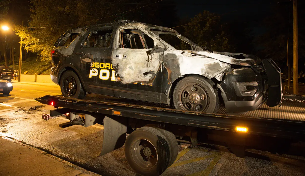 Mobil polisi Georgia berada di atas truk setelah dibakar pengunjuk rasa di depan kantor polisi di kampus di Atlanta, AS (18/9). Tiga orang ditangkap saat demonstrasi berlangsung. (Foto AP / Kevin D. Liles)