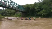 Jembatan sepanjang kurang lebih 50 meter ini ditutup karena sedang diperbaiki. Warga pun terpaksa menyeberang dengan rakit bambu meskipun arusnya deras dan dalam. (Liputan6.com/Darno)