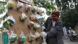 Seniman wayang uwuh, Iskandar Hardjodimuljo menggantungkan paket bahan makanan di jalan Cawang Baru Utara, Jakarta, Sabtu (18/4/2020). Paket bahan makanan yang diberi nama "Wayang Bersedekah" tersebut membantu warga yang kesulitan akibat dampak pandemi covid-19. (Liputan6.com/Herman Zakharia)