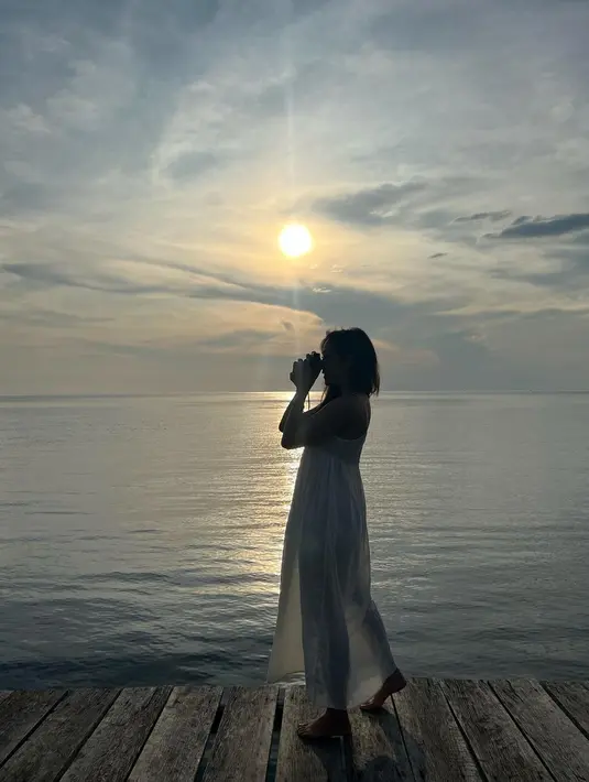 Seluruh keindahan alam dirasakan Gisella Anastasia saat liburan, termasuk matahari terbenam. Berlatar laut dan matahari yang hendak terbenam, Gisel mengenakan dress menerawang berwarna putih. Potret yang nyaris siluet ini menampilkan sosok Gisel yang sedang membidik objek dengan kamera.