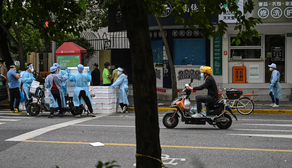 Pekerja yang mengenakan alat pelindung diri menumpuk kotak ke atas gerobak untuk dikirim saat perberlakuan lockdown karena virus corona COVID-19 di Distrik Jing'an, Shanghai, China, Rabu (18/5/2022). (Hector RETAMAL/AFP)