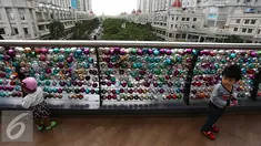 Anak-anak bermain di depan ribuan Bola bertuliskan harapan yang tergantung di pagar jembatan Eco Skywalk di Mall Central Park, Jakarta, Senin (19/12). Pengunjung dapat membeli Bola Pengharapan dengan harga Rp. 10.000. (Liputan6.com/Johan Tallo)