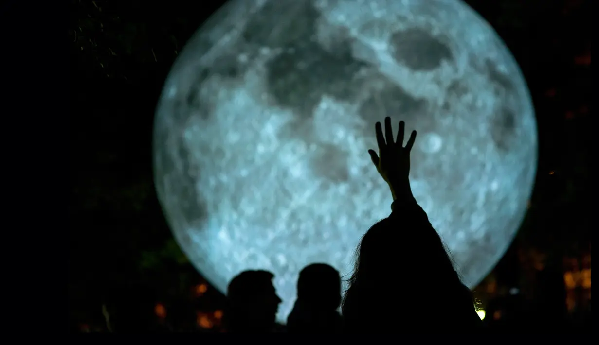 Seorang pengunjung berusaha menyentuh replika bulan raksasa yang dipajang di Bratislava, Slovakia, 7 Oktober 2017. Replika bulan tersebut merupakan karya seniman Inggris, Luke Jerram yang bertajuk 'Museum of The Moon'. (JOE KLAMAR / AFP PHOTO)