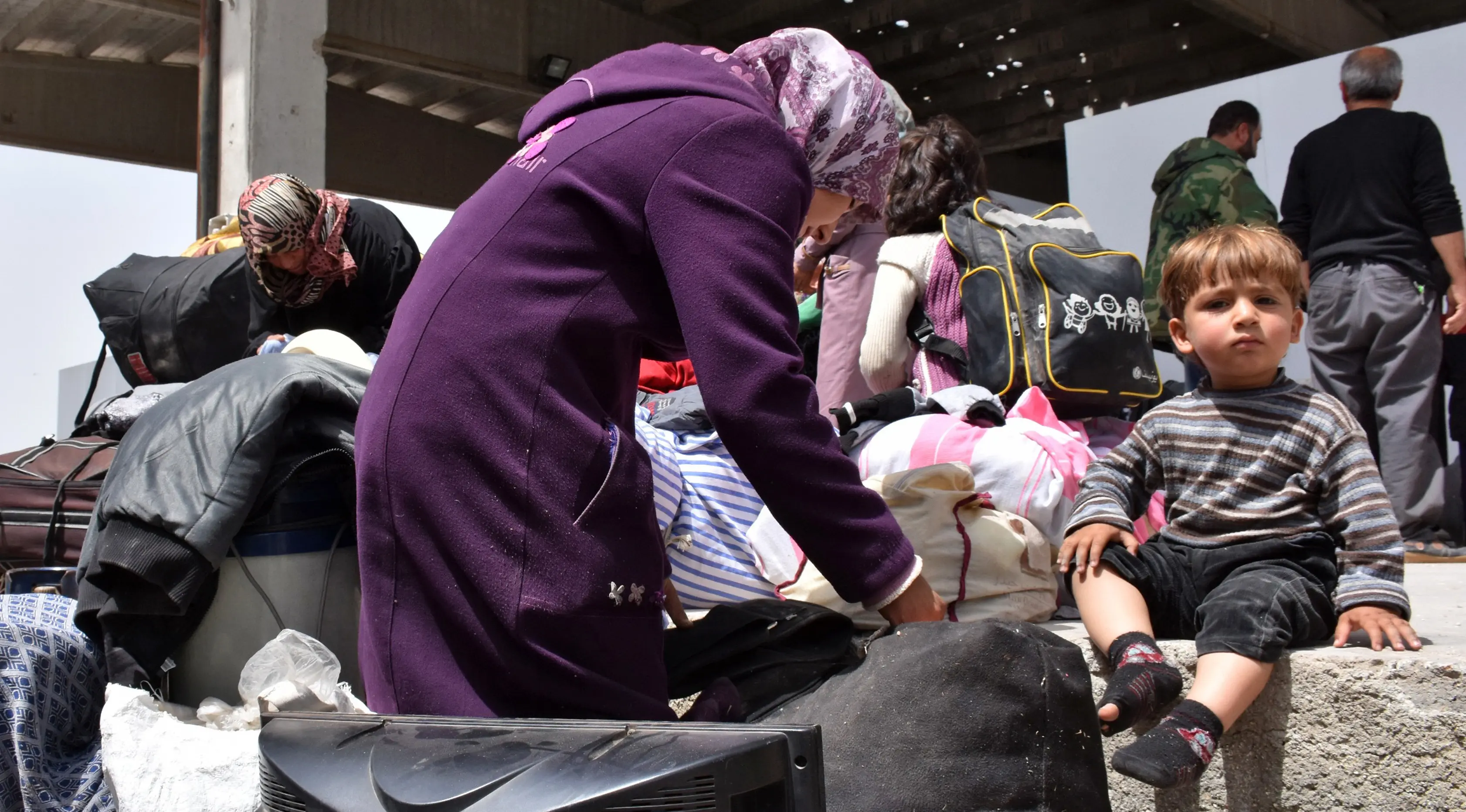 Seorang anak duduk di dekat ibunya saat sampai di sebuah tempat penampungan sementara di Jibrin di pinggiran timur Aleppo, Jumat (21/4). Pengungsi adalah warga dari kota Fuaa dan Kafraya. (AFP PHOTO / George OURFALIAN)