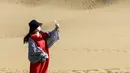 Seorang wisatawan berswafoto di kawasan wisata Gurun Kum Tag di Wilayah Shanshan, Kota Turpan, Daerah Otonom Uighur Xinjiang, China barat laut (22/9/2020). Gurun tersebut saat ini mencatat peningkatan arus wisatawan. (Xinhua/Wang Fei)