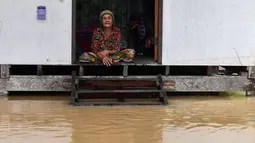 Seorang warga melihat banjir dari rumahnya di distrik Ran-ngea di provinsi Narathiwat, Thailand selatan (26/2/2022).  Hujan yang disebabkan oleh angin timur laut di atas Teluk Thailand terus berlanjut selama tiga hari berturut-turut di provinsi perbatasan selatan ini. (AFP/Madaree Tohlala)