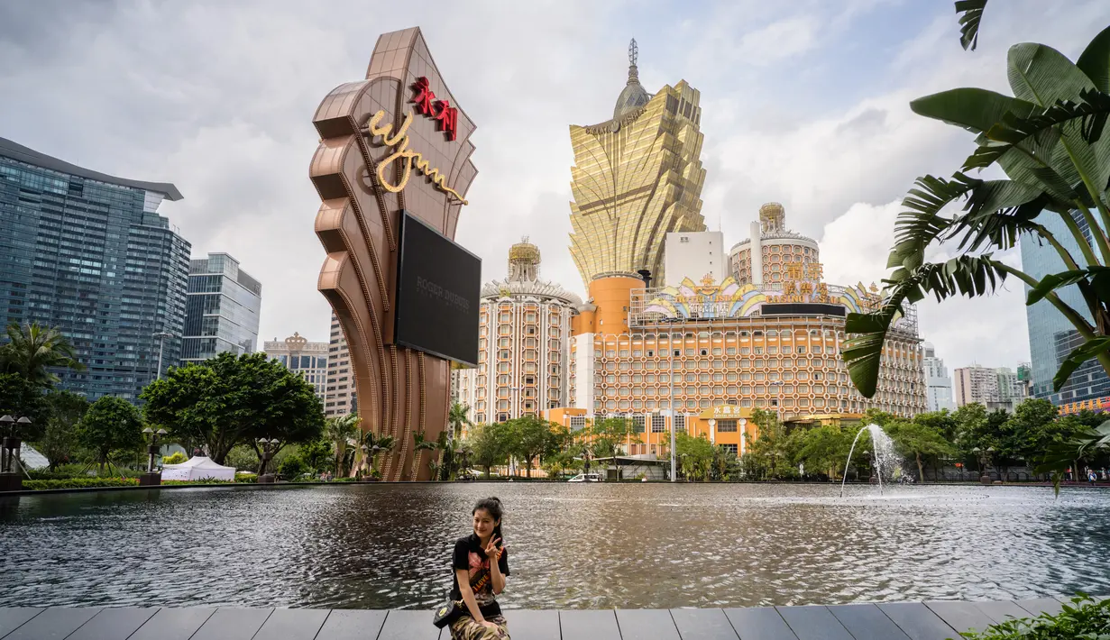 Wisatawan berpose dengan latar belakang resor kasino Grand Lisboa (tengah) di Macau, 5 Maret 2019. Macau menyimpan kasino-kasino ternama dan dicap sebagai surga bagi para penjudi. (Anthony Wallace/AFP)