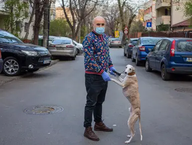 George Popa (51) berpose dengan anjing Ziggy (7) saat perjalanan di Bucharest (28/3/2020). Undang-undang militer, yang disahkan pemerintah Rumania untuk mengurangi penyebaran virus corona, menyatakan berjalan bersama anjing adalah salah satu  kegiatan yang masih diizinkan. (AFP/Andrei Pungovschi)