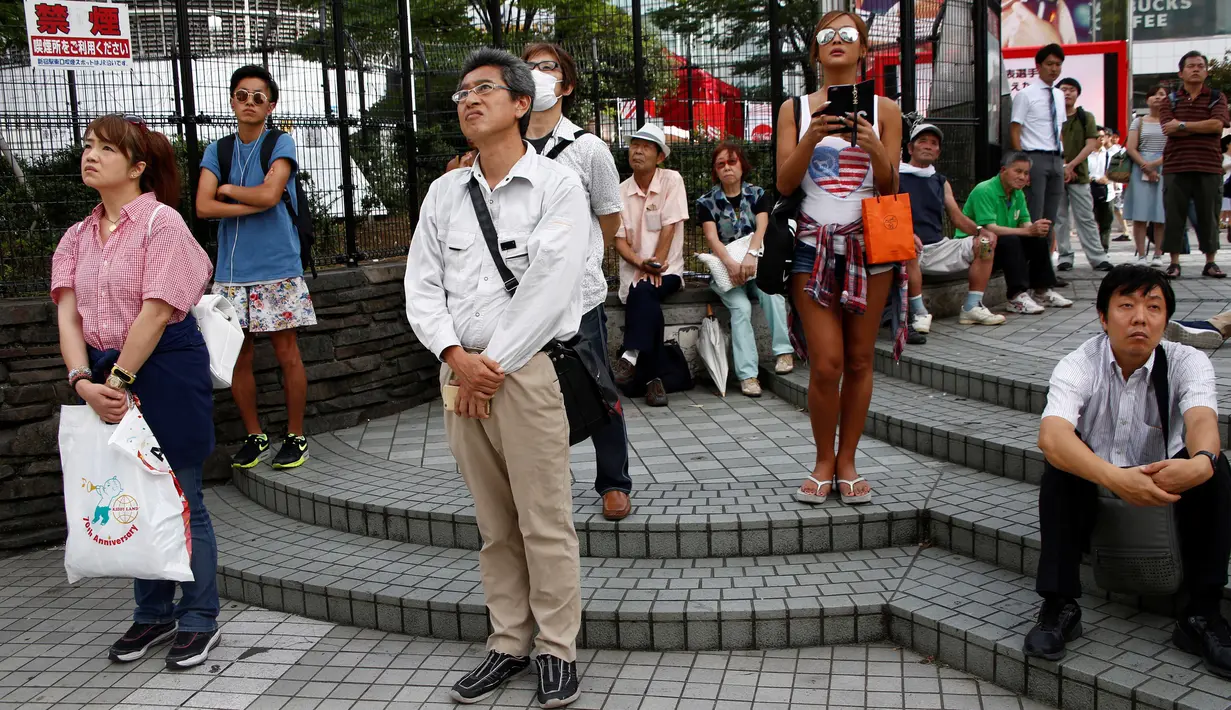 Sejumlah warga menyaksikan video pidato Kaisar Jepang Akihito, yang ditayangkan di layar lebar di Tokyo, Jepang. (8/8). Video rekaman pidato berdurasi 10 menit ini ditayangkan di stasiun televisi nasional. (REUTERS/Kim Kyung-Hoon)