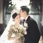 Mengenakan gaun pengantin yang elegan dan tiara mewah, Lee Da In memegang karangan bunga dan tersenyum cerah, sementara suaminya Lee Seung Gi, mengenakan tuksedo di sampingnya, berpose dengan tangan di sakunya dan mencium keningnya. [Foto: IG/byhumanmade]