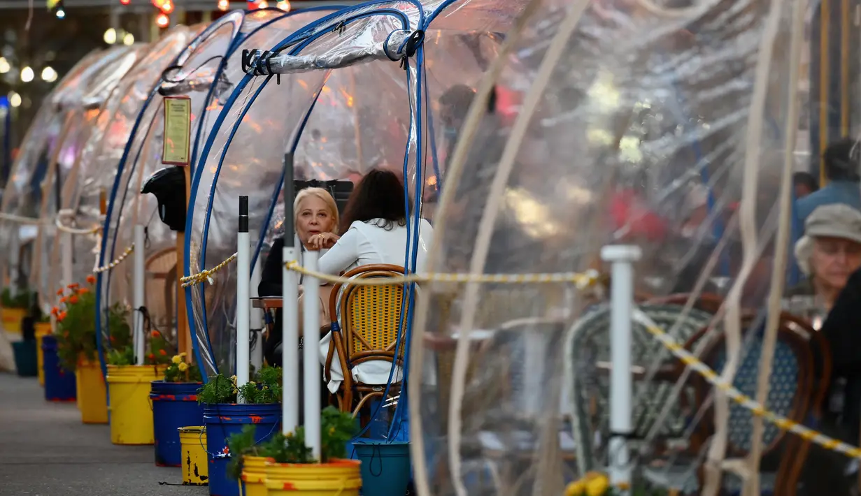 Orang-orang menikmati makanan di dalam tenda plastik untuk menjaga jarak di sebuah restoran di Manhattan, New York City, Kamis (15/10/2020). Konsep gelembung luar angkasa ini menawarkan sensasi tersendiri sekaligus berjaga-jaga dari resiko penularan COVID-19 bagi para pelanggan. (Angela Weiss/AFP)