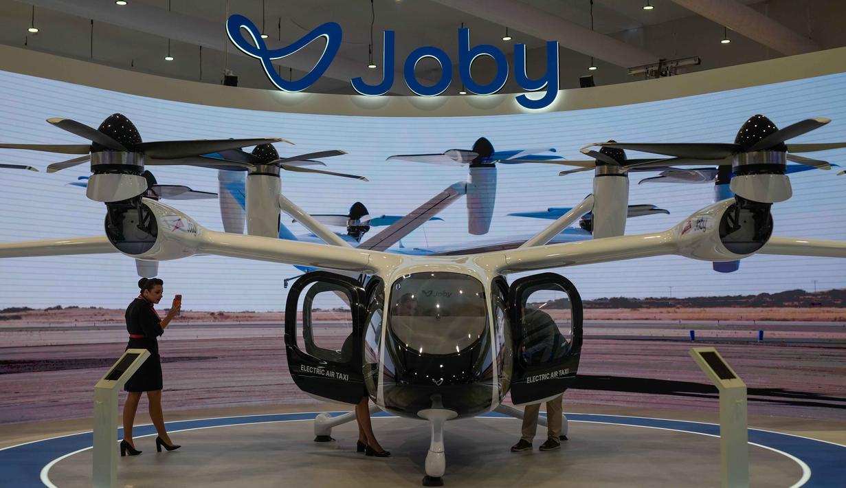 Adalah Joby Aviation Inc. perusahaan asal Amerika Serikat, tengah melakukan rangkaian uji terbang untuk pesawat taksi udara berbasis baterai mereka di Margham menuju Bandara Internasional Al Maktoum, Uni Emirat Arab. Tampak dalam foto, seorang wanita mengambil foto taksi udara Dubai yang dipamerkan pada Pameran Udara Dubai, Uni Emirat Arab, Selasa 18 November 2025. (AP Photo/Altaf Qadri)
