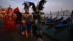 Sejumlah peserta mengenakan topeng dan kostum unik berdiri di St Mark Square selama Karnaval Venesia di Italia, Sabtu (27/1). Karnaval Venesia digelar 40 sebelum Paskah. (FILIPPO MONTEFORTE / AFP)