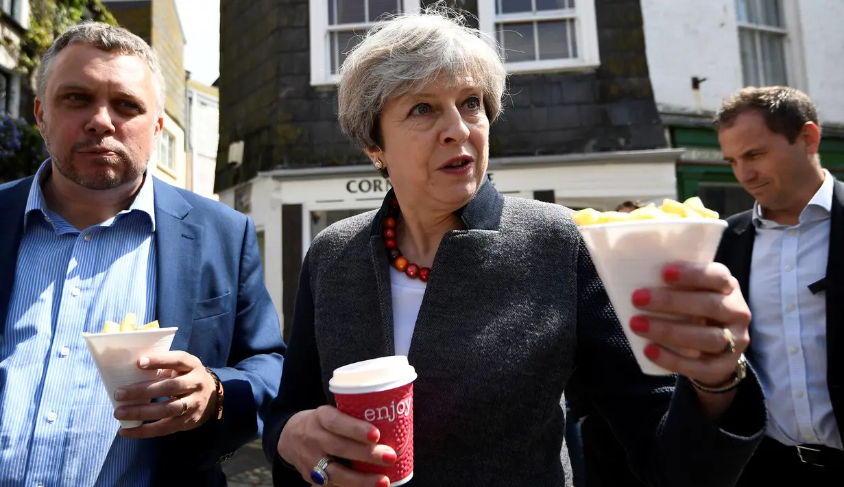 Perdana Menteri (PM), Inggris Theresa May membawa sebungkus keripik saat menemui warga disela kampanyenya di Mevagissey, Cornwall, Selasa (2/5). Theresa May melakukan kampanye dengan berkeliling jalanan di Cornwall. (AFP PHOTO/POOL/DYLAN MARTINEZ)