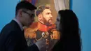 Pengunjung berbincang dekat lukisan megabintang Argentina, Lionel Messi pada Piala Dunia 2018 di Museum of Academy of Arts, Saint Petersburg, Rusia, Rabu (20/6). Para bintang sepak bola dunia dilukis layaknya seorang jenderal militer. (AP/Dmitri Lovetsky)