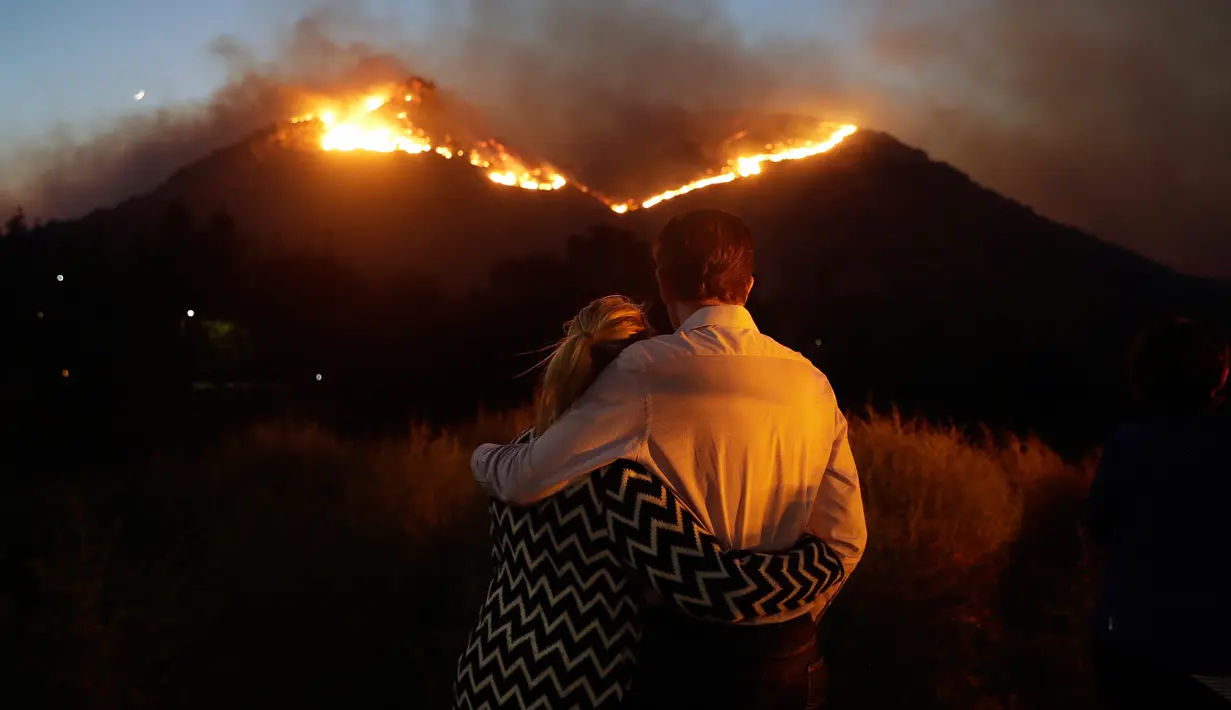 Roger Bloxberg dan istrinya, Anne berpelukan saat menyaksikan kebakaran di puncak bukit dekat rumah mereka di West Hills, California, AS, Jumat (9/11). Api Woolsey melahap ribuan hektare hutan dan menghancurkan banyak rumah. (AP Photo/Marcio Jose Sanchez)
