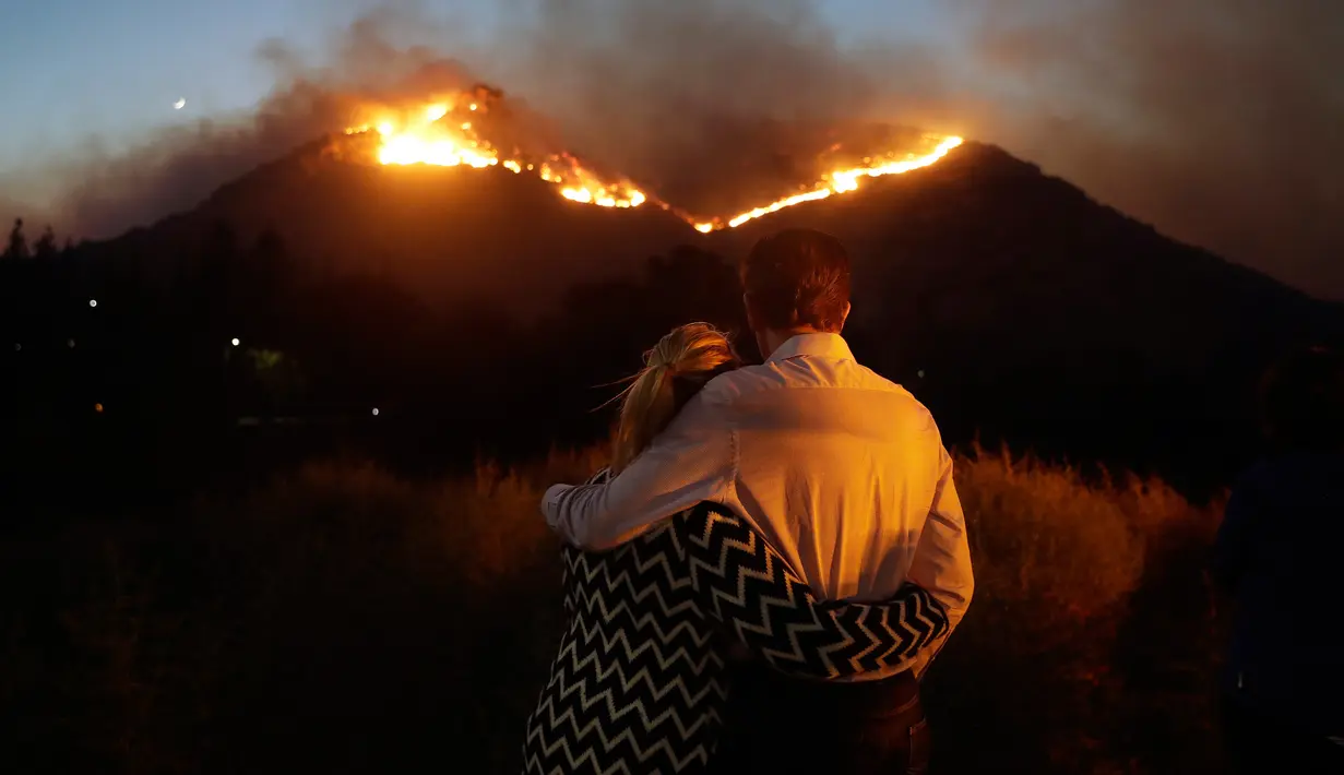 Roger Bloxberg dan istrinya, Anne berpelukan saat menyaksikan kebakaran di puncak bukit dekat rumah mereka di West Hills, California, AS, Jumat (9/11). Api Woolsey melahap ribuan hektare hutan dan menghancurkan banyak rumah. (AP Photo/Marcio Jose Sanchez)