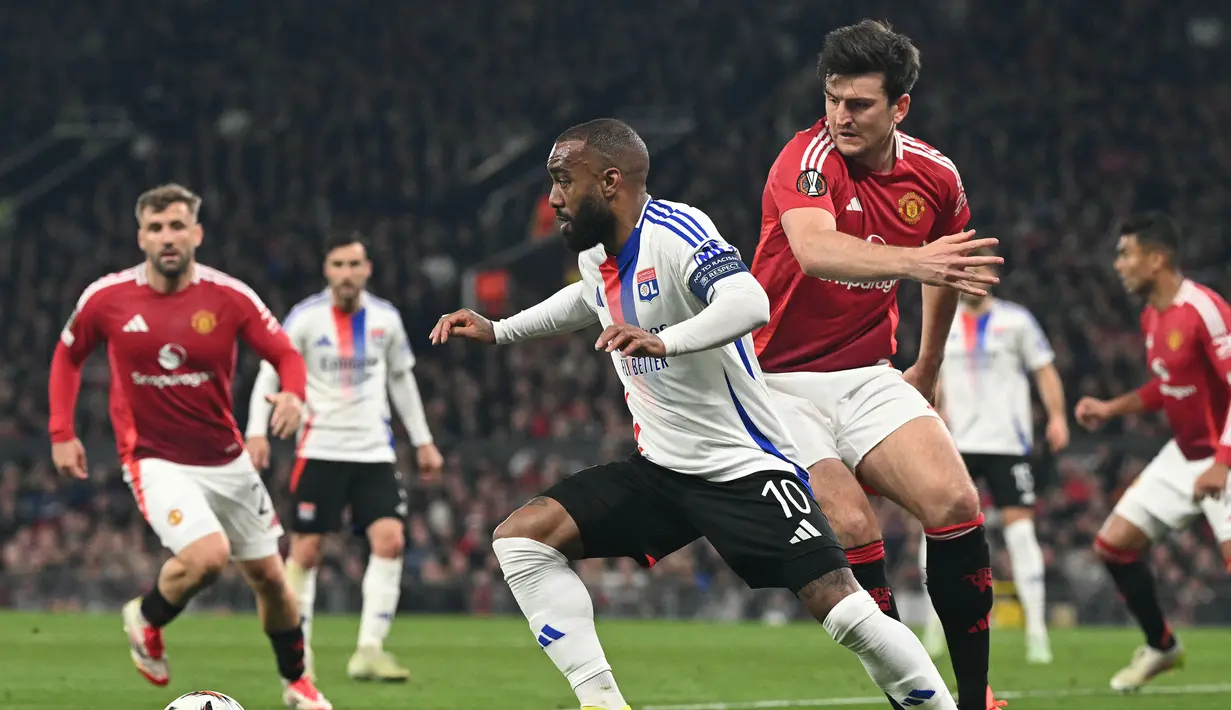 Pemain Manchester United, Harry Maguire berusaha merebut bola dari kaki pemain Lyon, Alexandre Lacazette dalam laga leg 2 perempat final Liga Europa 2024/2025 di Old Trafford, Manchester, Inggris, Jumat (18/04/2025) WIB. (AFP/Oli Scarff)