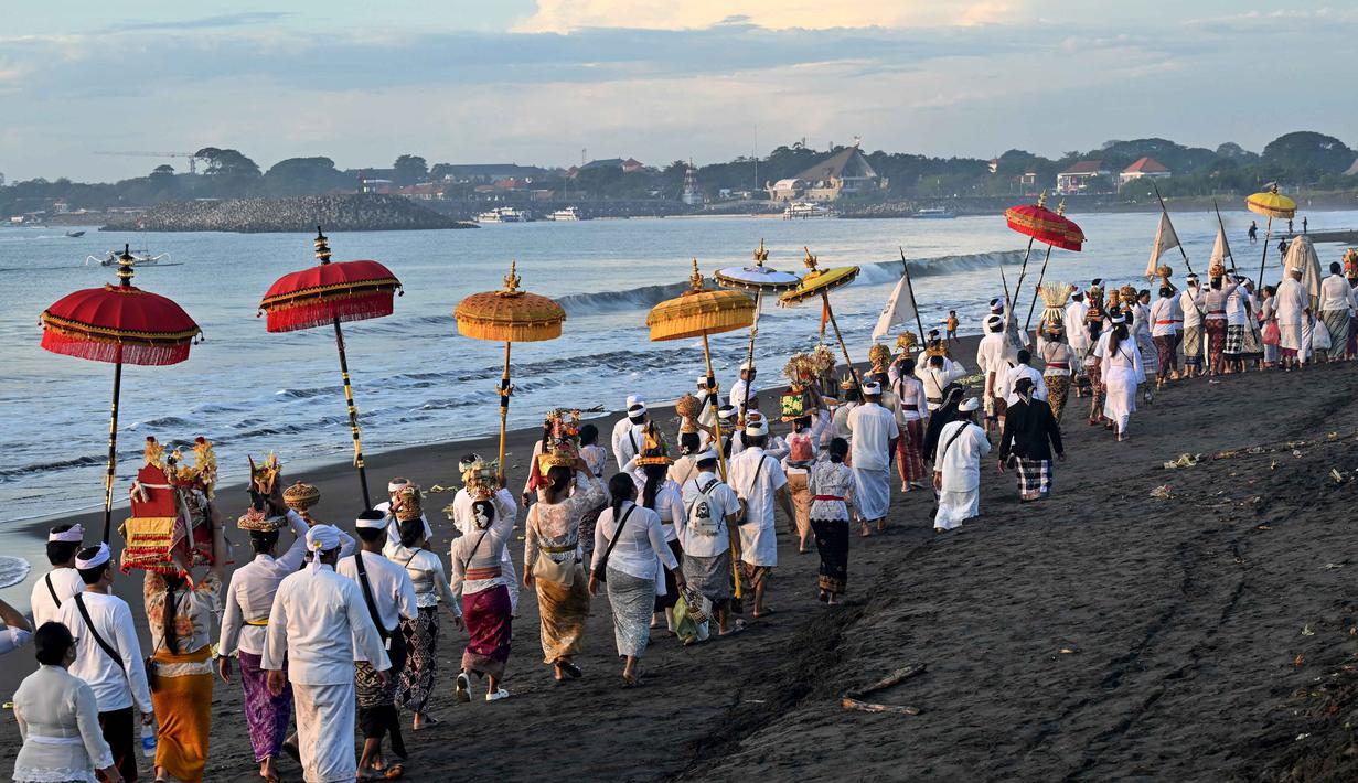 Prosesi ini berlangsung khidmat sebagai upaya penyucian simbol-simbol suci sebelum Nyepi. Tampak dalam foto, umat Hindu saat mengikuti upacara doa Melasti di salah satu pantai di Denpasar, Bali, pada Senin 16 Maret 2026. (SONNY TUMBELAKA/AFP)