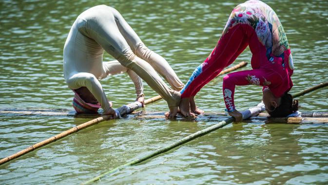 Orang-orang melakukan aksi meniti satu bambu di atas air di Chishui, Provinsi Guizhou, China pada 25 Juni 2020. Seni meniti satu bambu berasal dari Guizhou ini mengharuskan seseorang untuk berdiri atau duduk di atas sebatang bambu sembari melakukan gerakan keseimbangan. (Xinhua/Tao Liang)