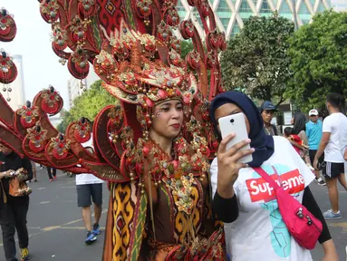 Seorang warga yang tengah mengikuti Car Free Day (CFD) berswafoto dengan peserta Parade Asian Games 2018 2018 di Jalan Thamrin, Jakarta, Minggu (13/5). Tak merasa terganggu, mereka justru ikut antusias menyaksikan parade itu. (Liputan6.com/Arya Manggala)