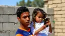 Houra bermain ponsel saat digendong saudaranya di desa Wahed Haziran, Provinsi Diwaniya, Irak, (17/3). Penyakit langka ini membuat Houra rentan terserang kanker kulit paling berbahaya, yakni melanoma. (AFP Photo/Haidar Hamdani)