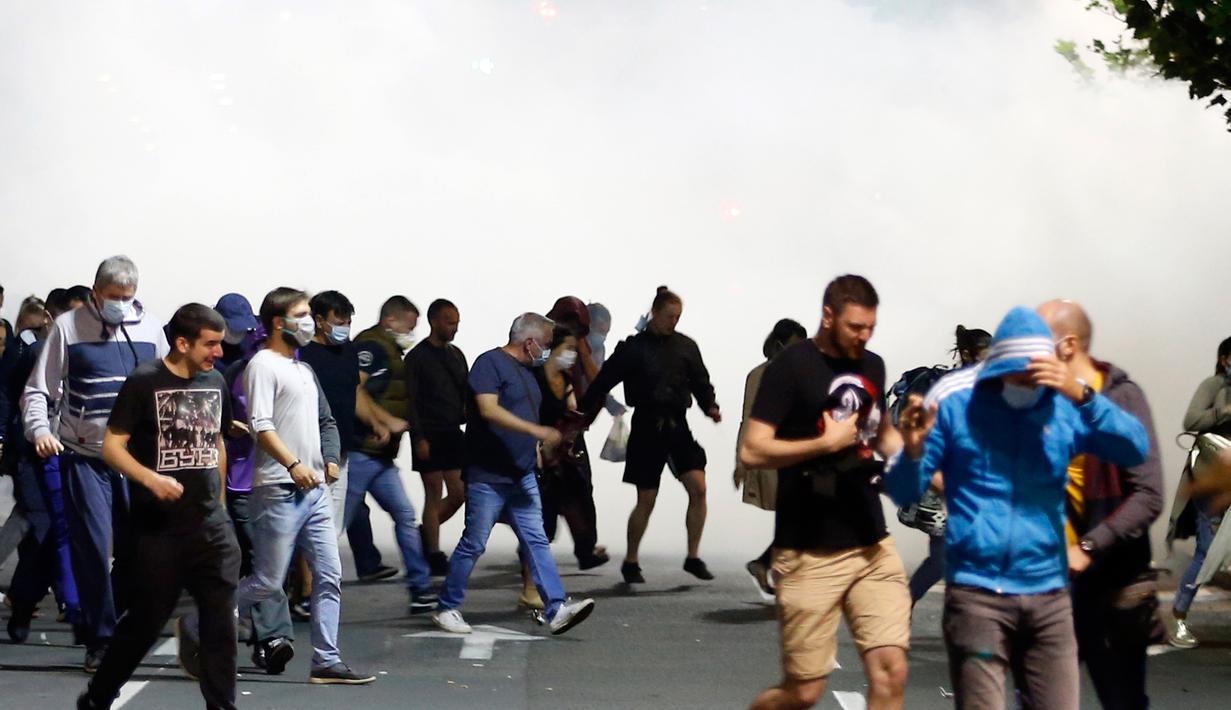 Para pengunjuk rasa lari dari gas air mata di depan gedung parlemen Serbia di Beograd, Selasa (7/7/2020). Ribuan pengunjuk rasa marah setelah pemerintah mengeluarkan keputusan untuk memberlakukan kembali jam malam akibat melonjaknya kasus Covid-19. (AP/Marko Drobnjakovic)