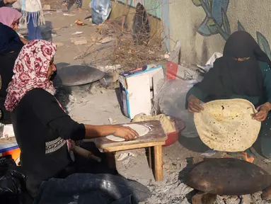 Para wanita Palestina membuat roti tidak beragi tradisional di atas api terbuka di salah satu lokasi penampungan pengungsi pada 27 Oktober 2023. (SAID KHATIB/AFP)
