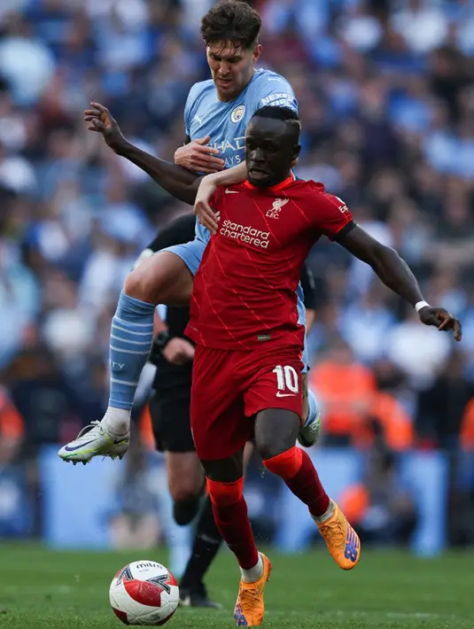 Pemain Manchester City John Stones (kiri) berebut bola dengan pemain Liverpool Sadio Mane pada pertandingan sepak bola semifinal Piala FA di Stadion Wembley, London, Inggris, 16 April 2022. Liverpool menang 3-2. (Adrian DENNIS/AFP)
