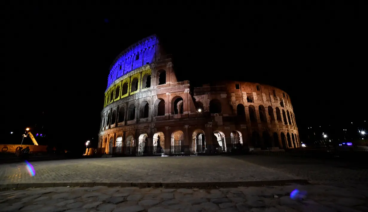 Pandangan umum ini menunjukkan Coliseum di Roma diterangi dengan warna bendera Ukraina, di Italia pada 24 Februari 2022. Warna kuning dan biru menerangi salah satu destinasi wisata paling ikonik di Roma tersebut sebagai solidaritas setelah invasi Rusia ke Ukraina. (Filippo MONTEFORTE / AFP)